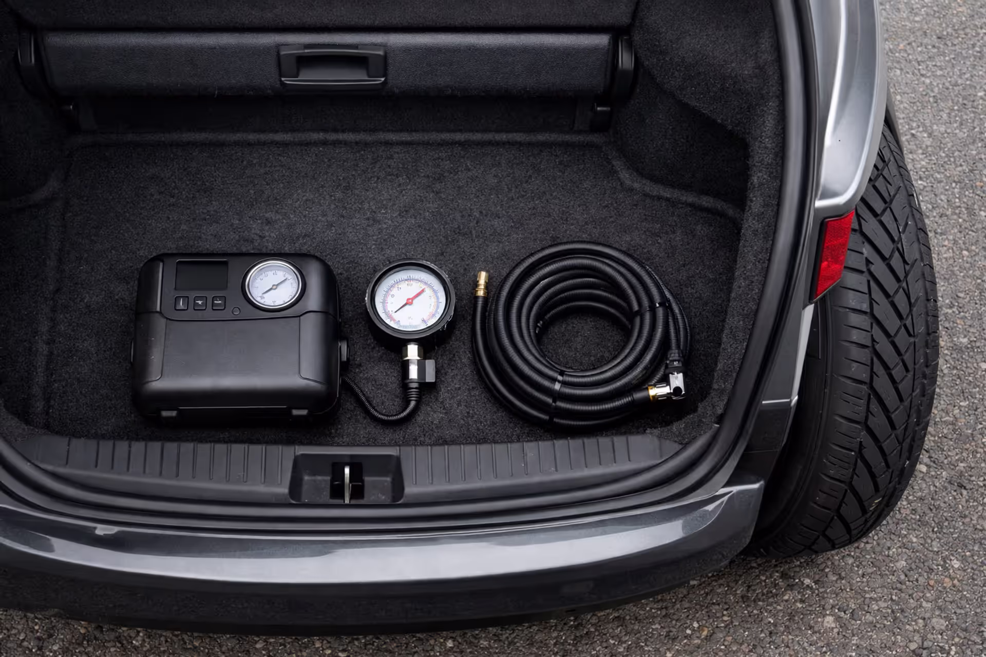 Portable tire inflator with pressure gauge stored in a car trunk next to a rear wheel